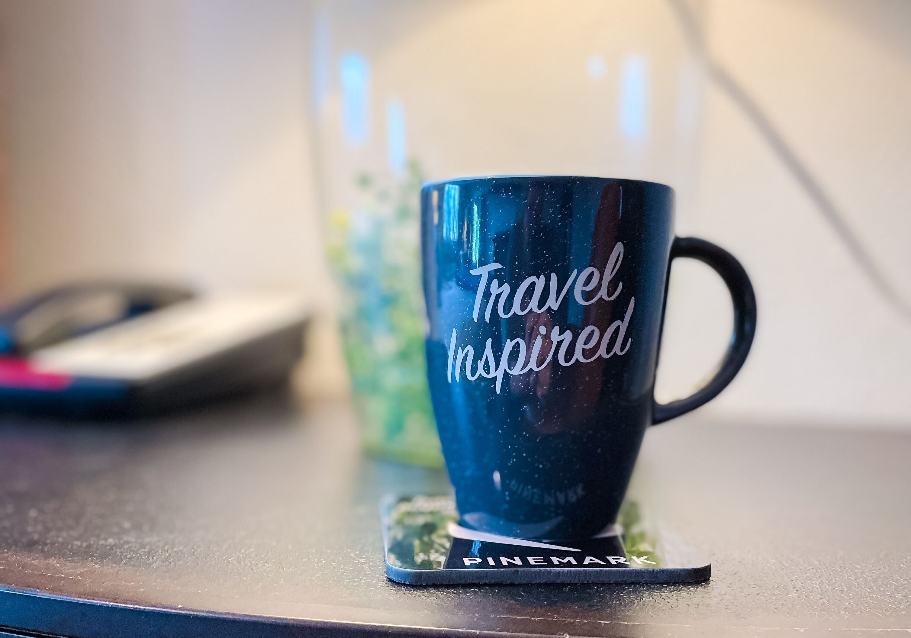 A dark blue mug with "Travel Inspired" text on a coaster.