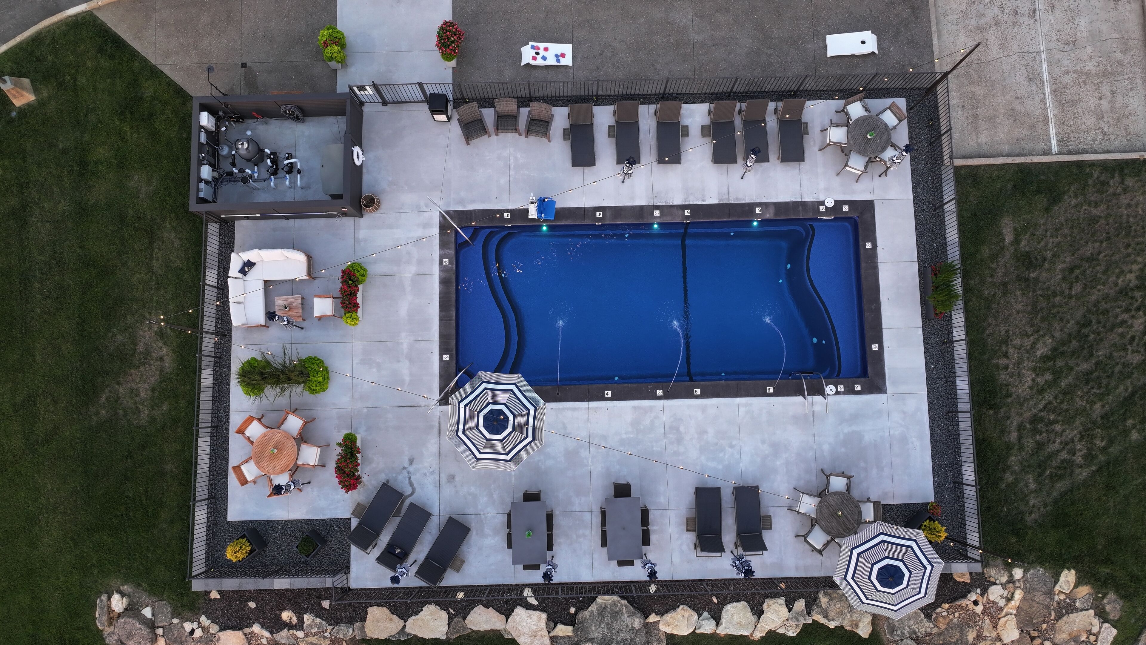 An aerial view of a swimming pool area with lounge chairs, umbrellas, and a barbecue setup.