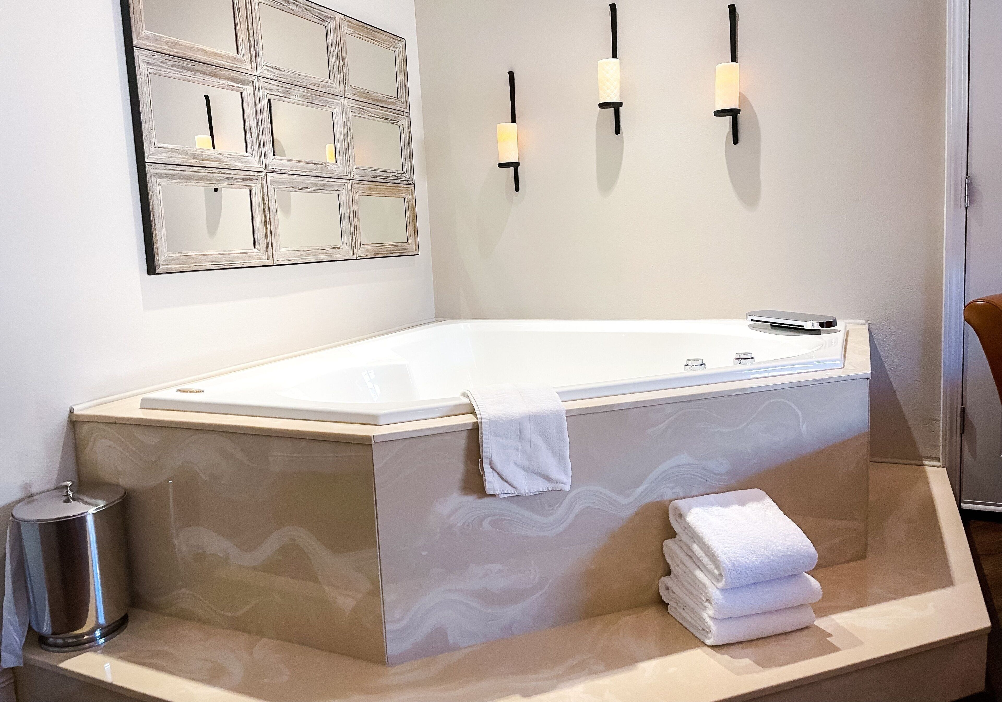 A modern bathroom with a freestanding bathtub, a marble vanity, a trash can, and a wall-mounted light fixture.