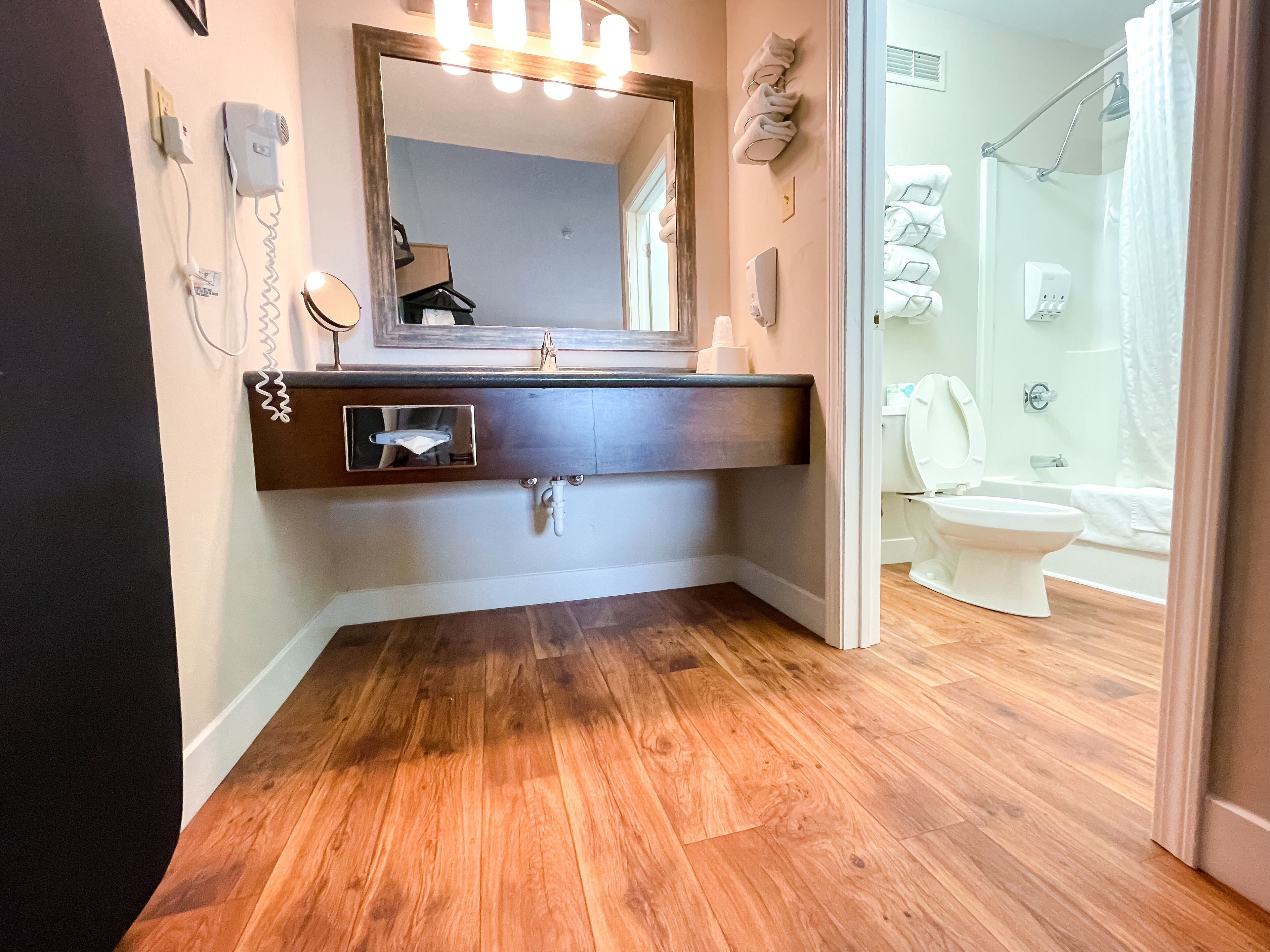 A bathroom with a wooden floor, a dark vanity with a mirror, and a white toilet.