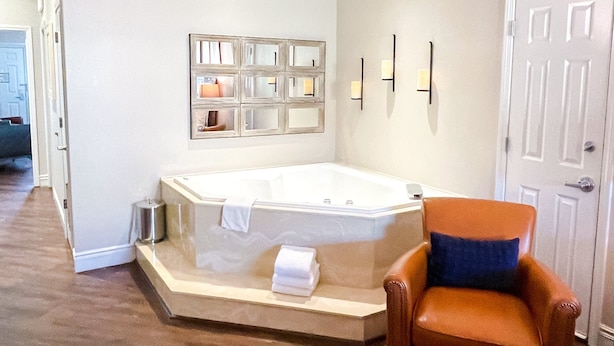 Un baño con una bañera grande, una silla y un estante pequeño con plantas.