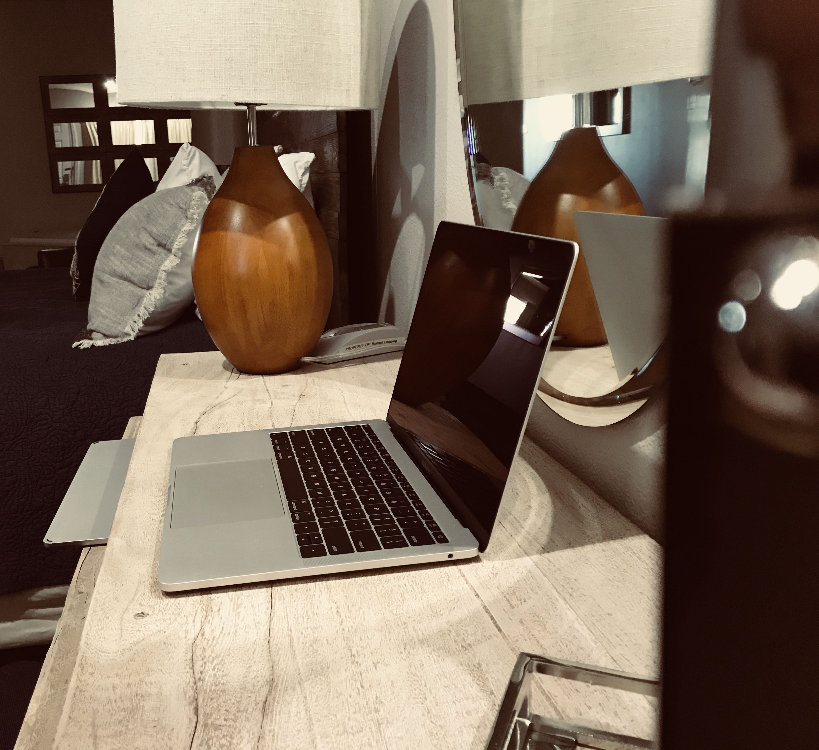 A laptop on a wooden table with a vase and a lamp in the background.