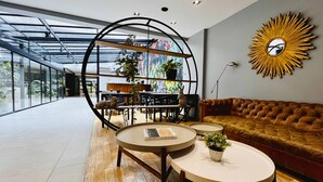 Un intérieur moderne avec un coin repas délimité par des parois de verre, un canapé en cuir marron et un miroir décoratif en forme de soleil rayonnant.