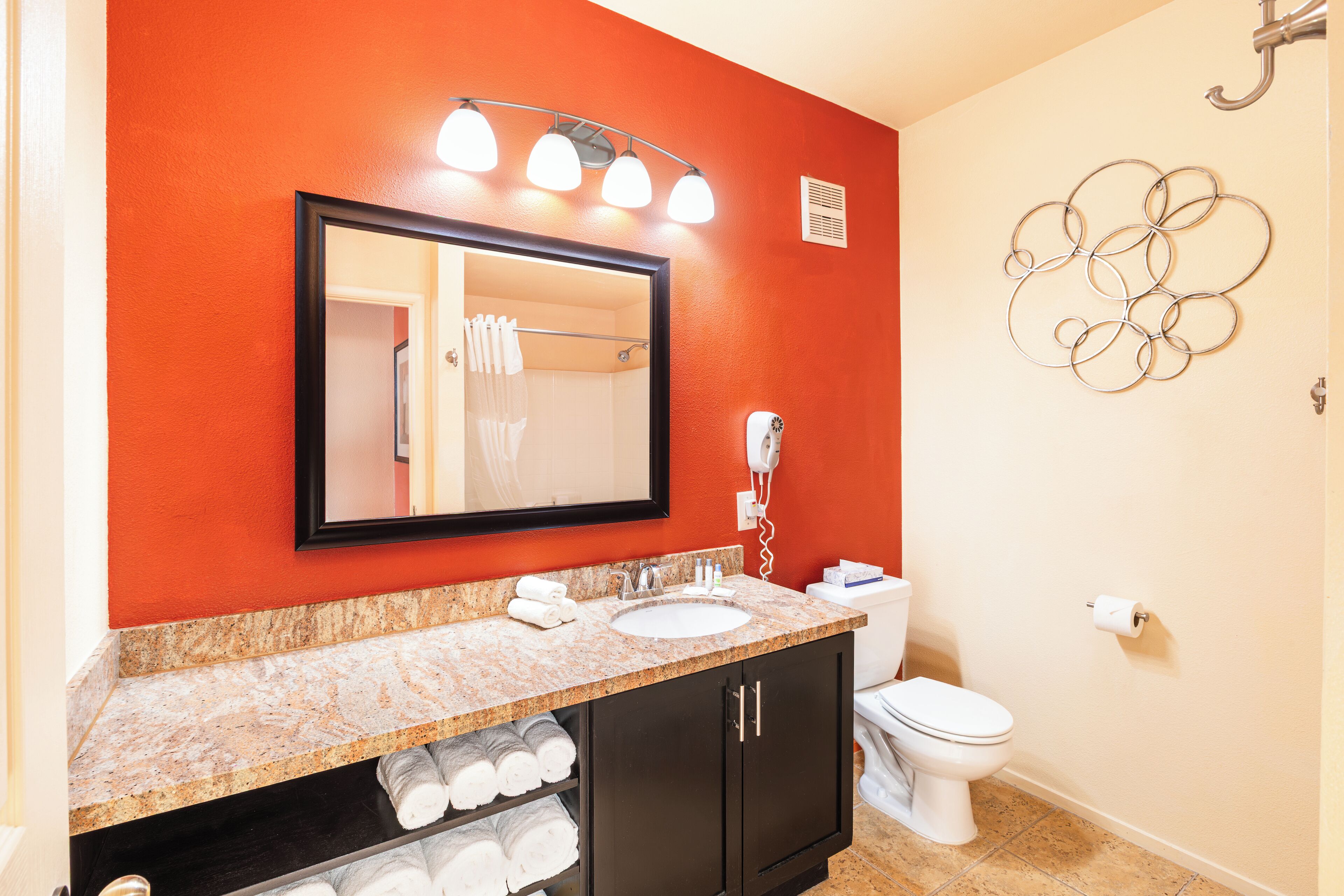 Une salle de bain avec un mur rouge, un lavabo, un miroir et des toilettes.