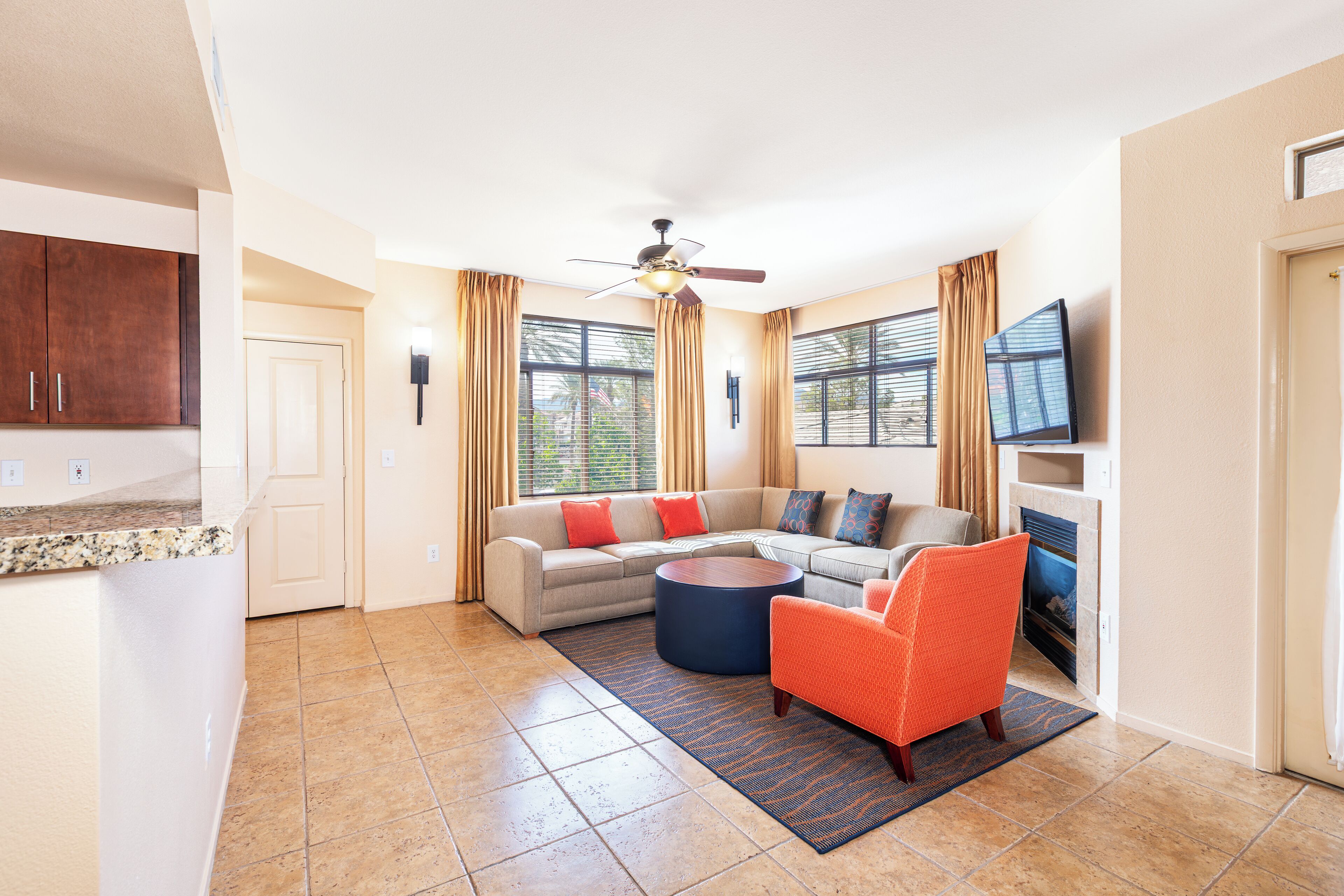A spacious living room with a large L-shaped sectional sofa, a round coffee table, and a bright ceiling fan.