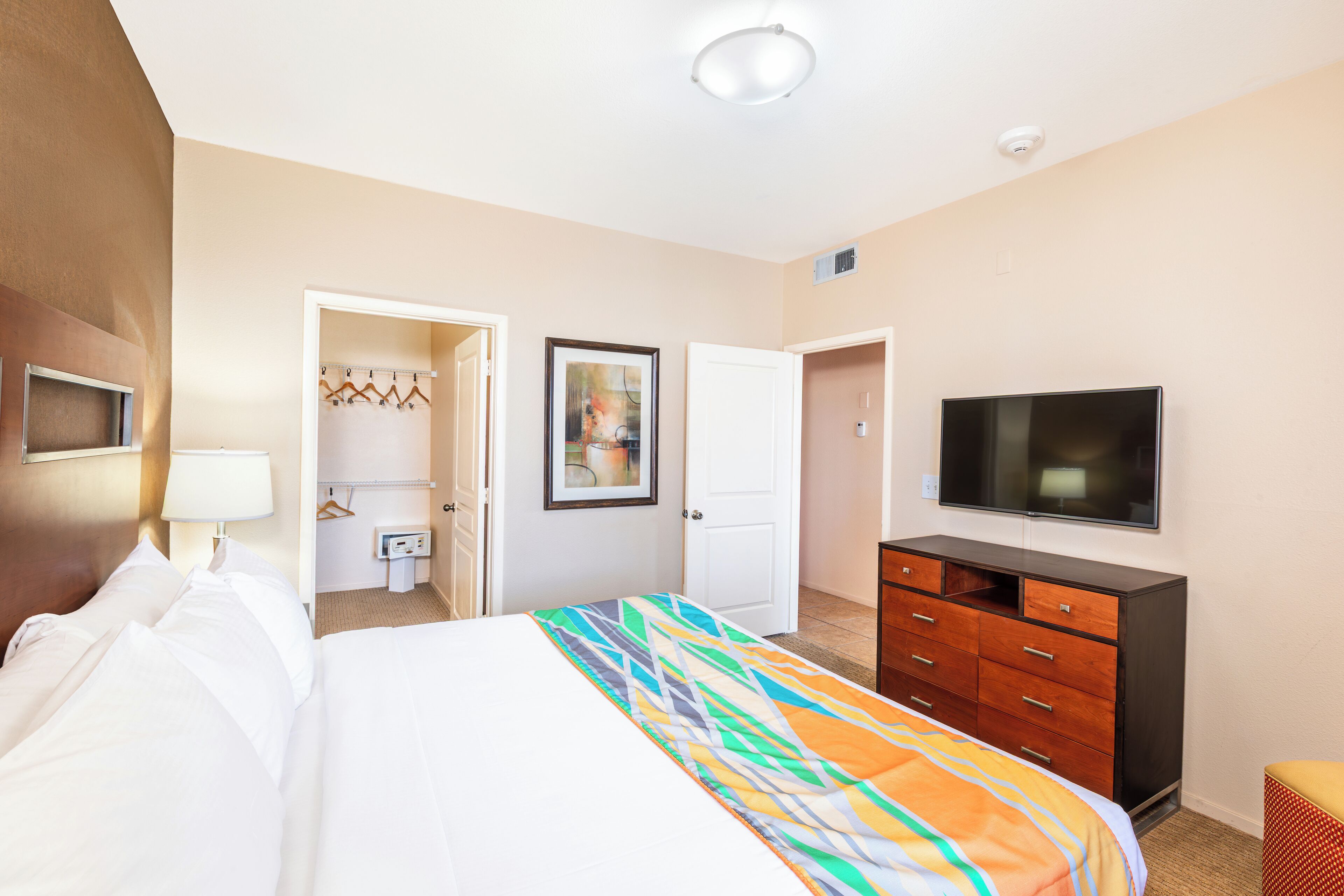 A hotel room with a bed, a dresser, a television, and a door leading to a bathroom.