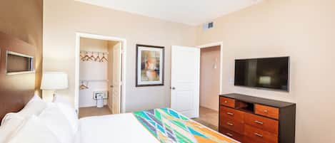 A hotel room with a bed, a dresser, a television, and a door leading to a bathroom.