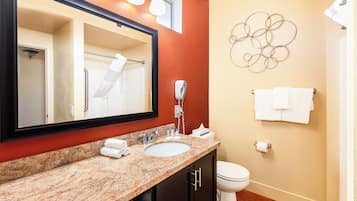 A bathroom with a granite countertop sink, a mirror, a toilet, and a towel rack.