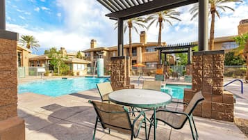 A pool area with a table and chairs, palm trees, and a covered seating area.