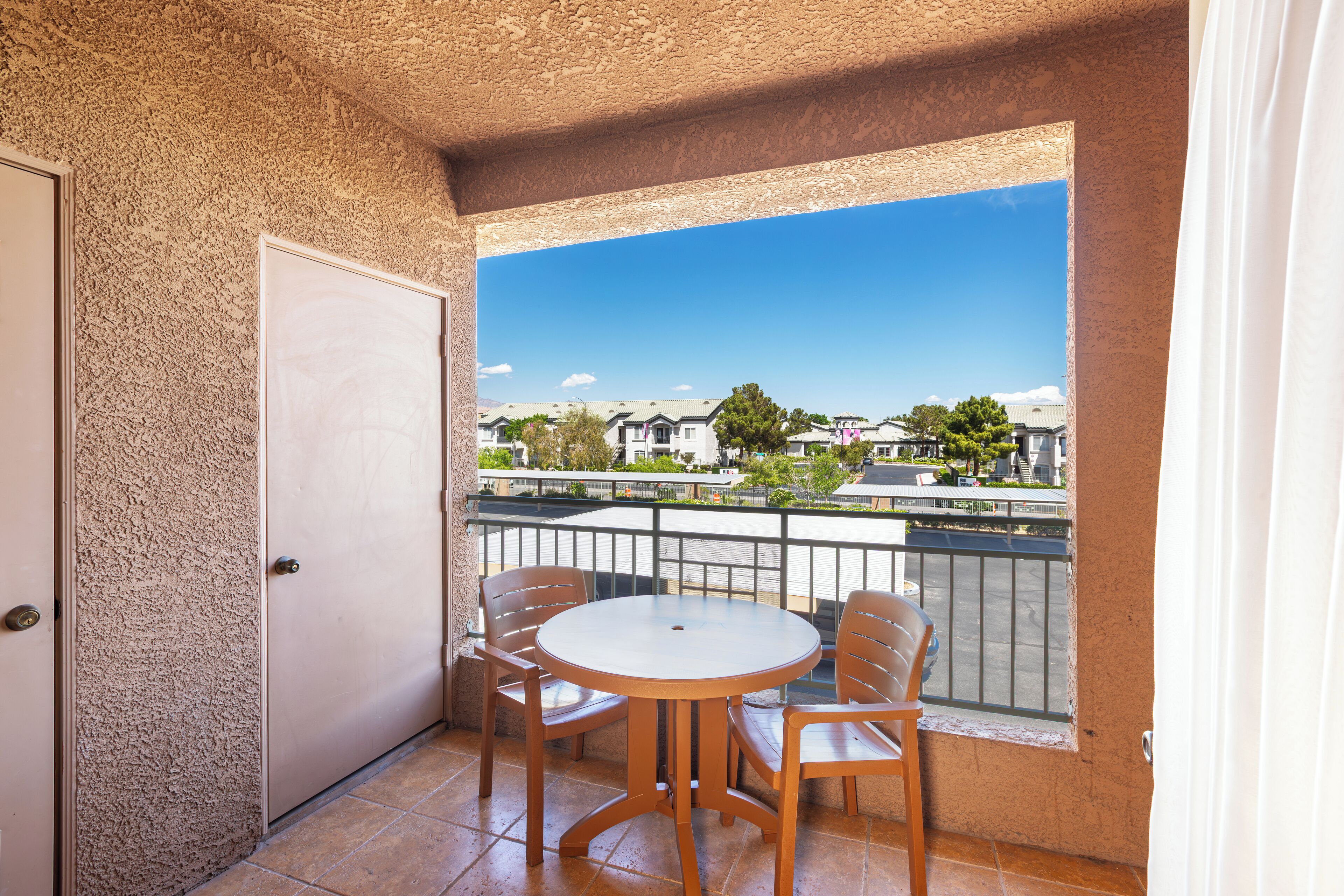 Un balcon avec une table ronde et des chaises, une vue sur des maisons et une porte.