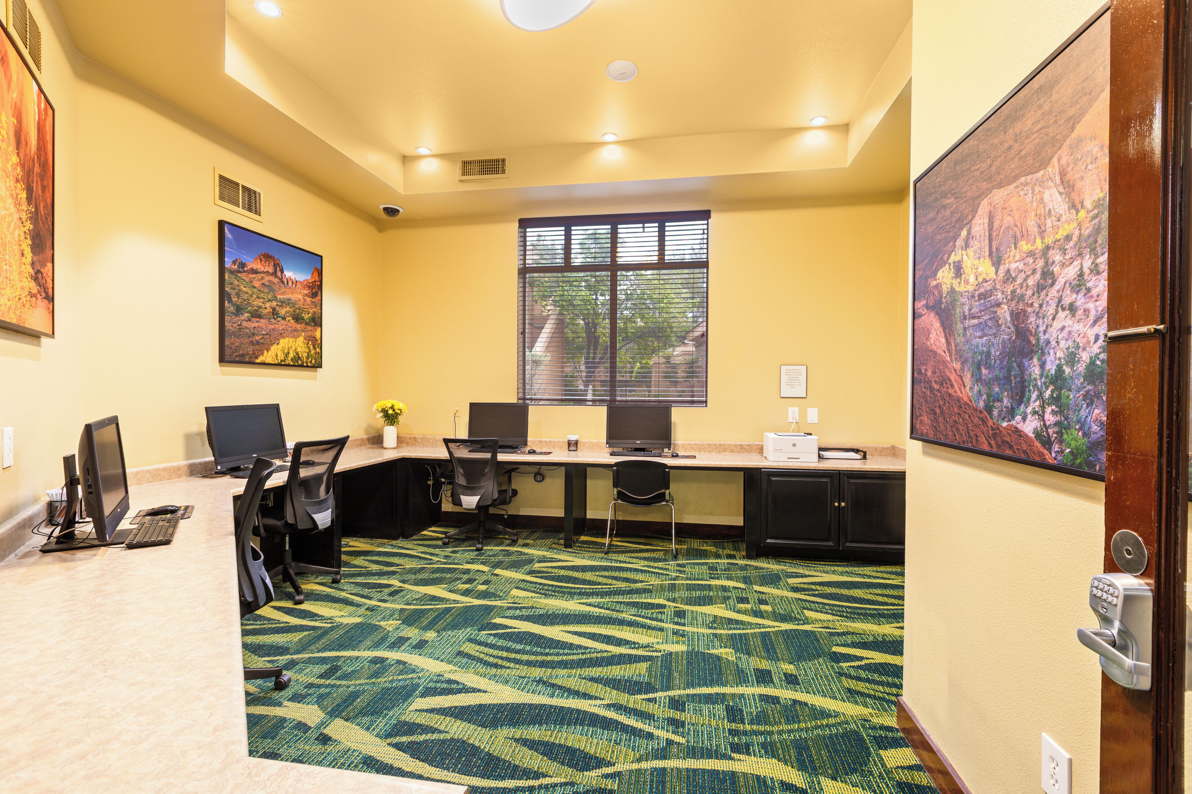A conference room with a carpeted floor, two desks with computers, chairs, and framed pictures on the walls.
