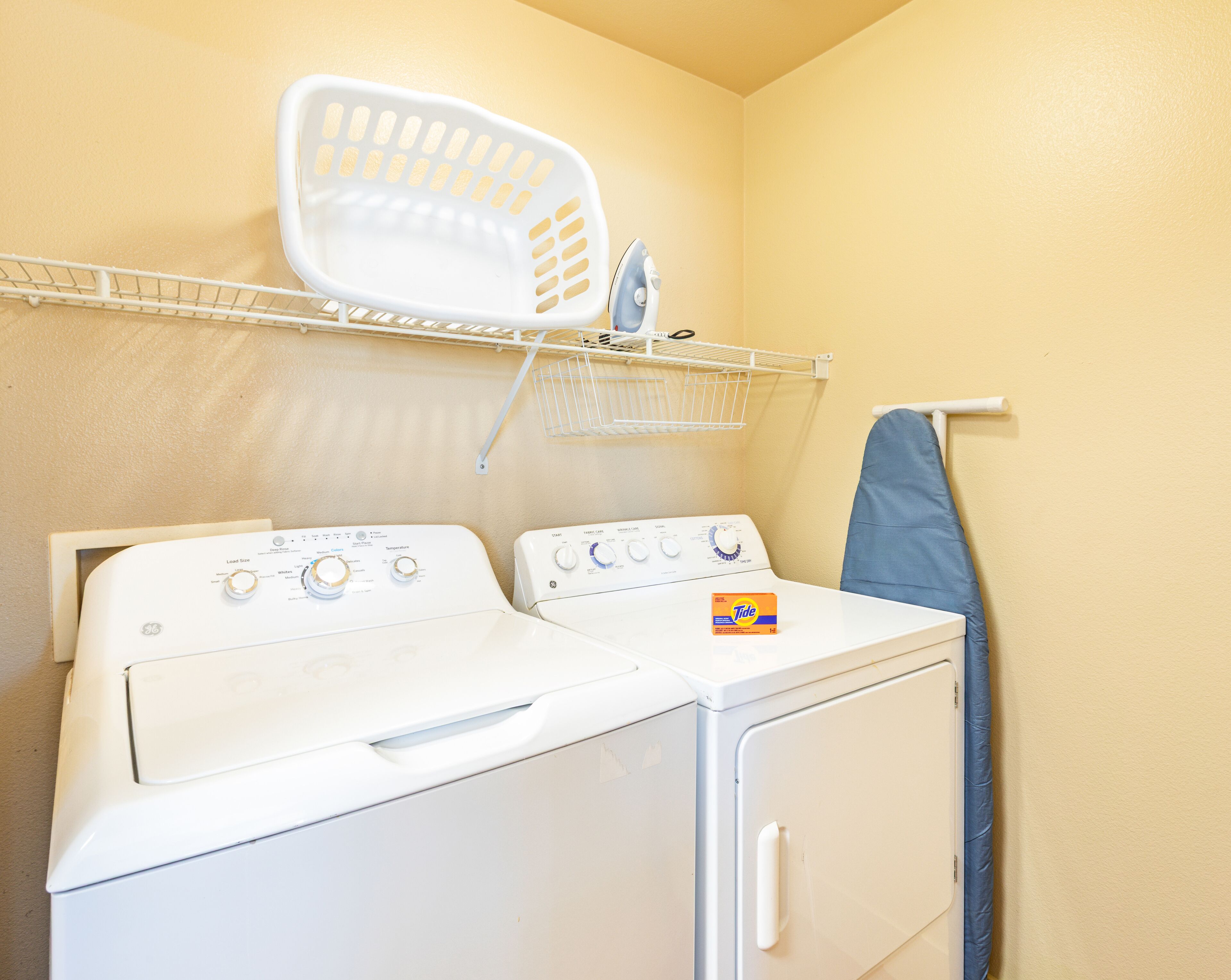 A laundry area with two stacked washers and dryers, a drying rack, and a hanging blue towel.
