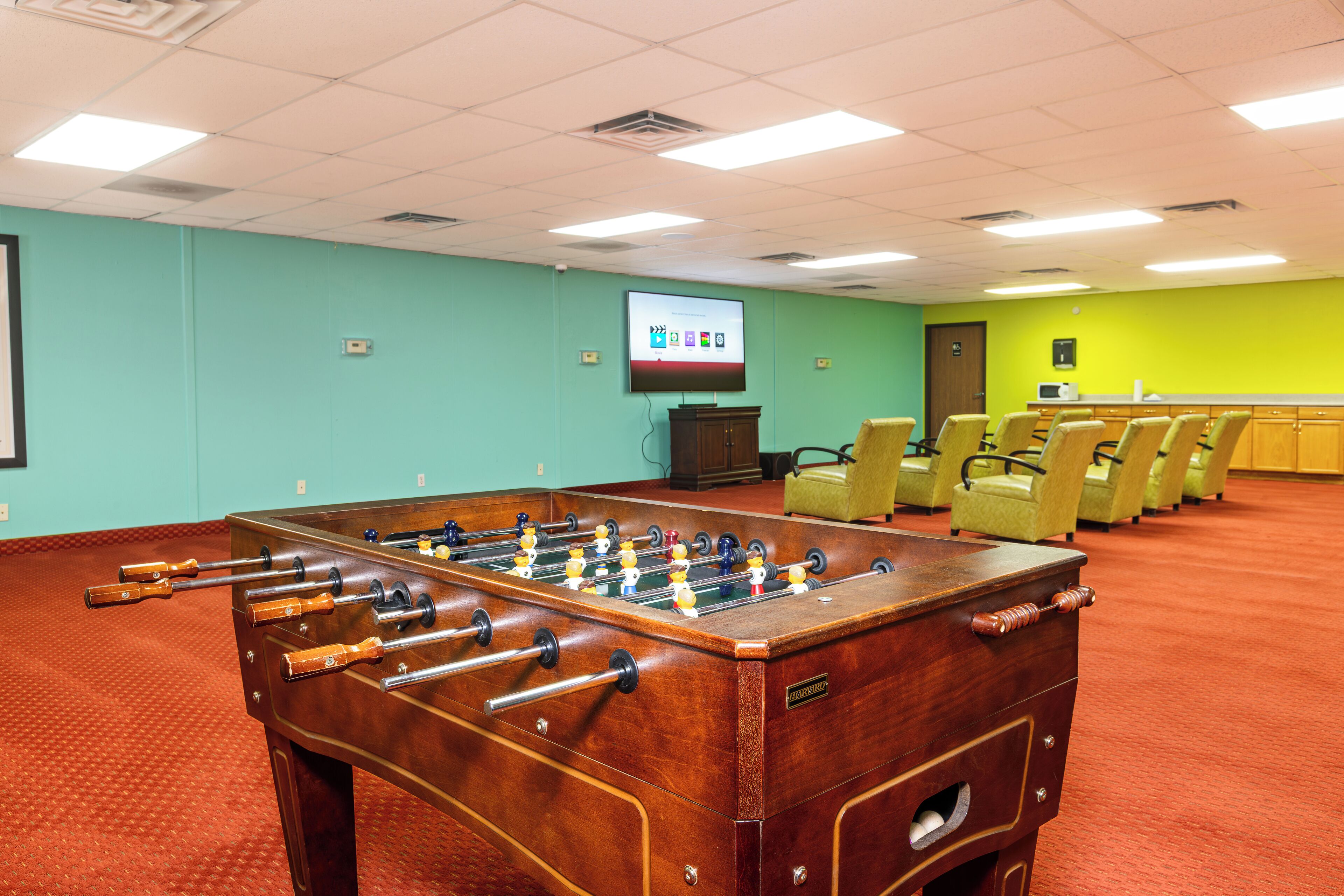 A room with a foosball table, a projection screen, and several chairs.