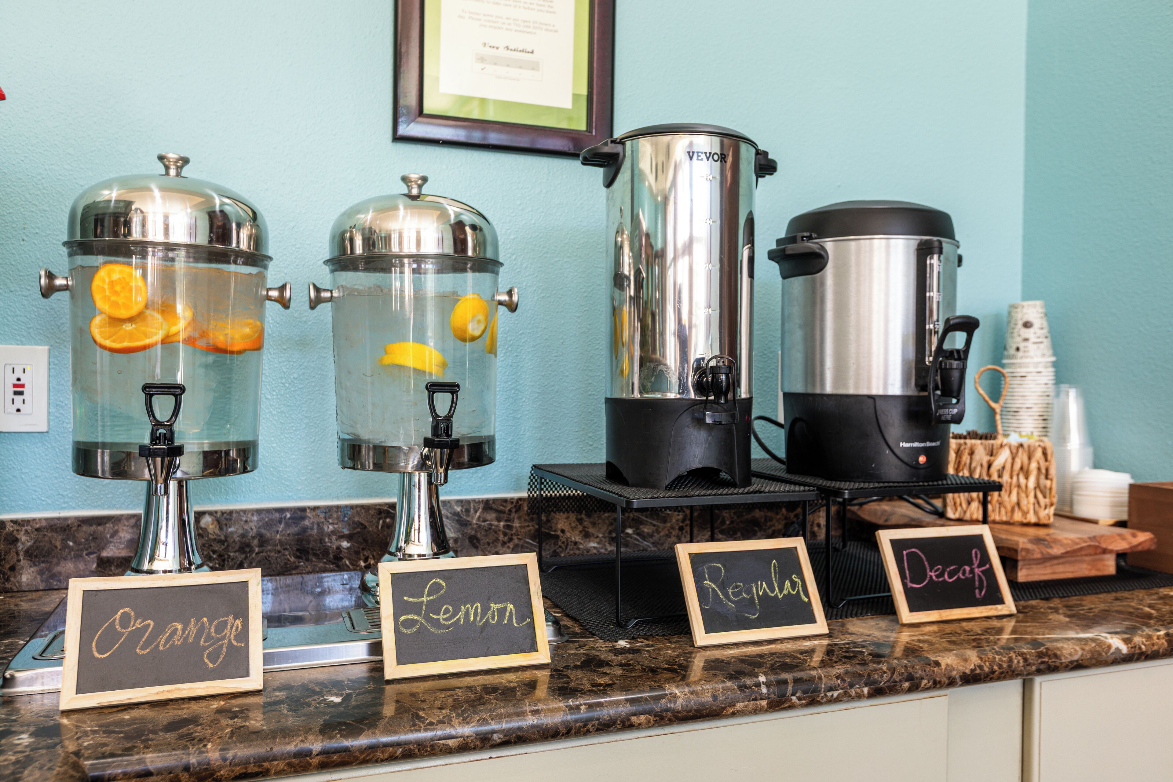 Una estación de café con dispensadores etiquetados para café de naranja, limón, normal y descafeinado.