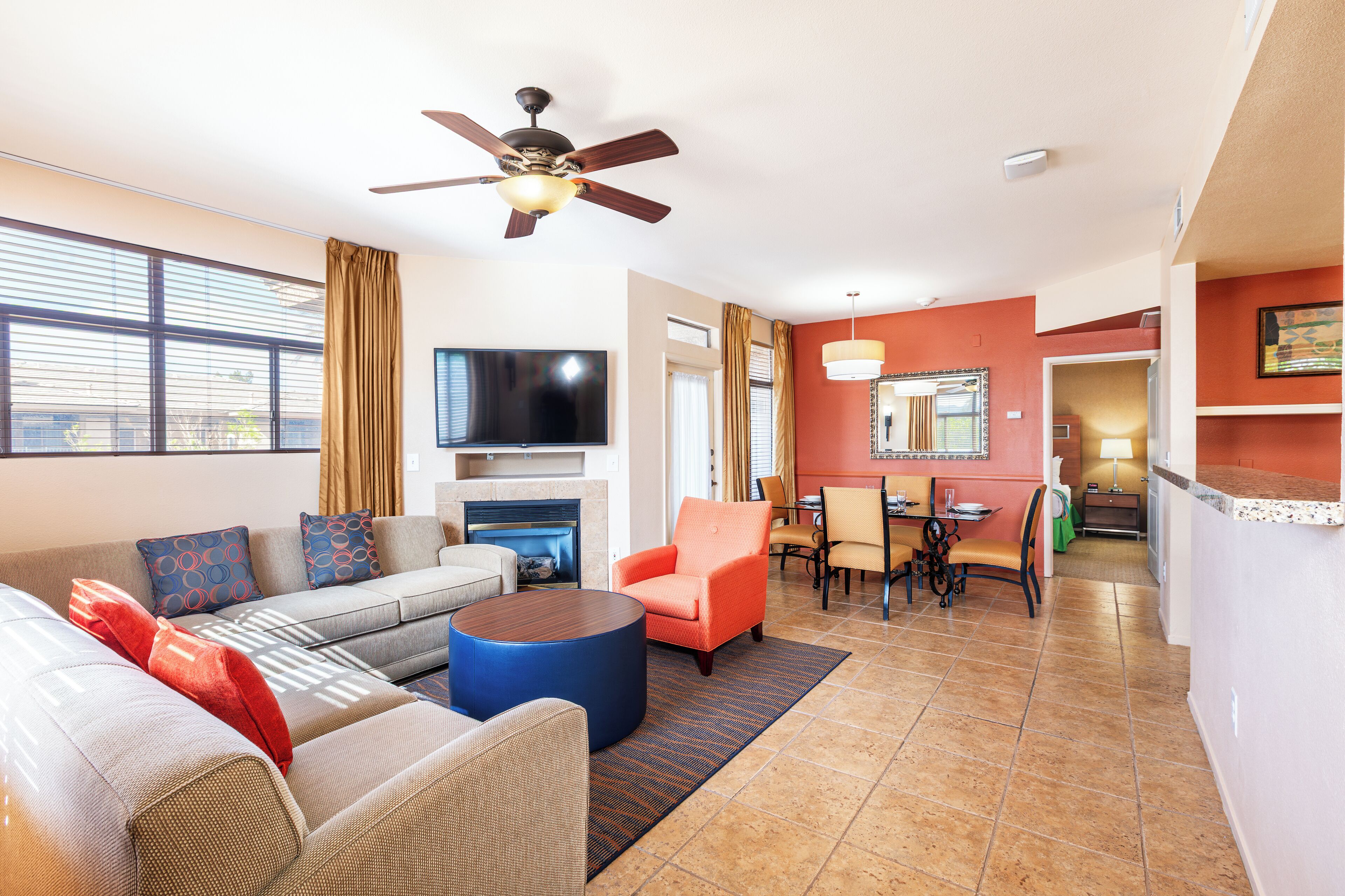 A modern living room with a flat-screen TV, a ceiling fan, and a dining area with a table and chairs.