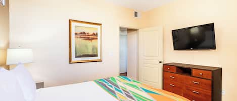 Una habitación de hotel con cama, televisión, cómoda y un cuadro en la pared.