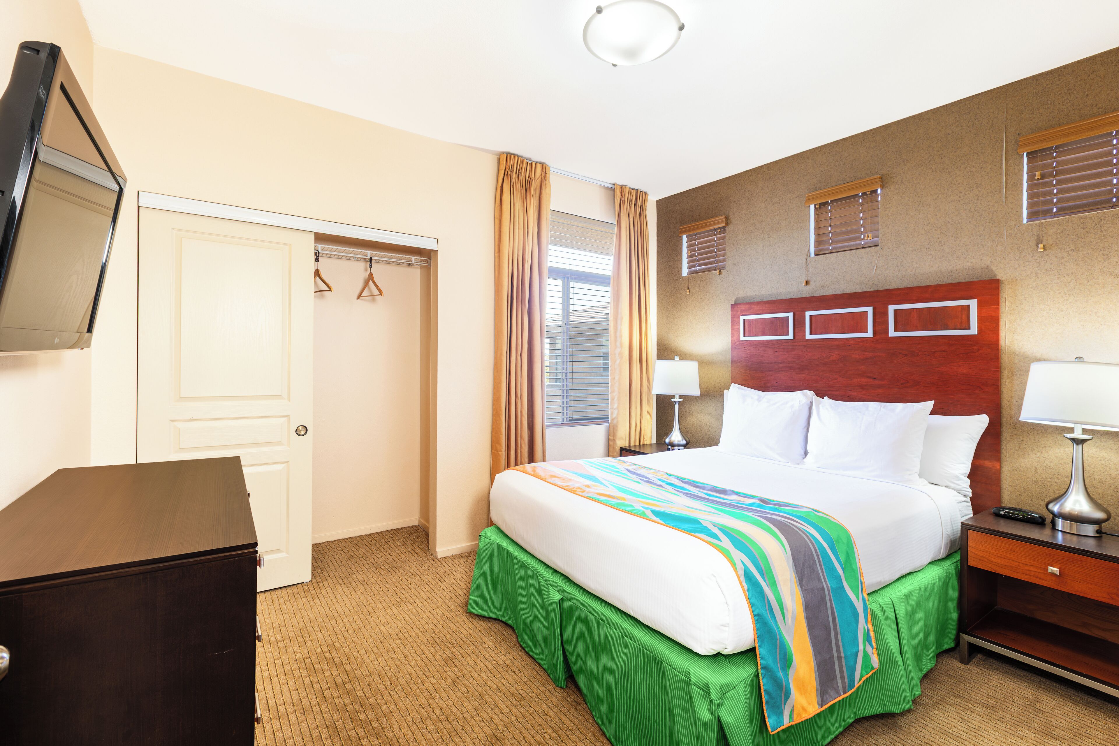 A hotel room with a bed, a dresser, a desk, and a TV.
