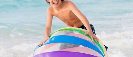 A person on a beach with a colorful striped ball.