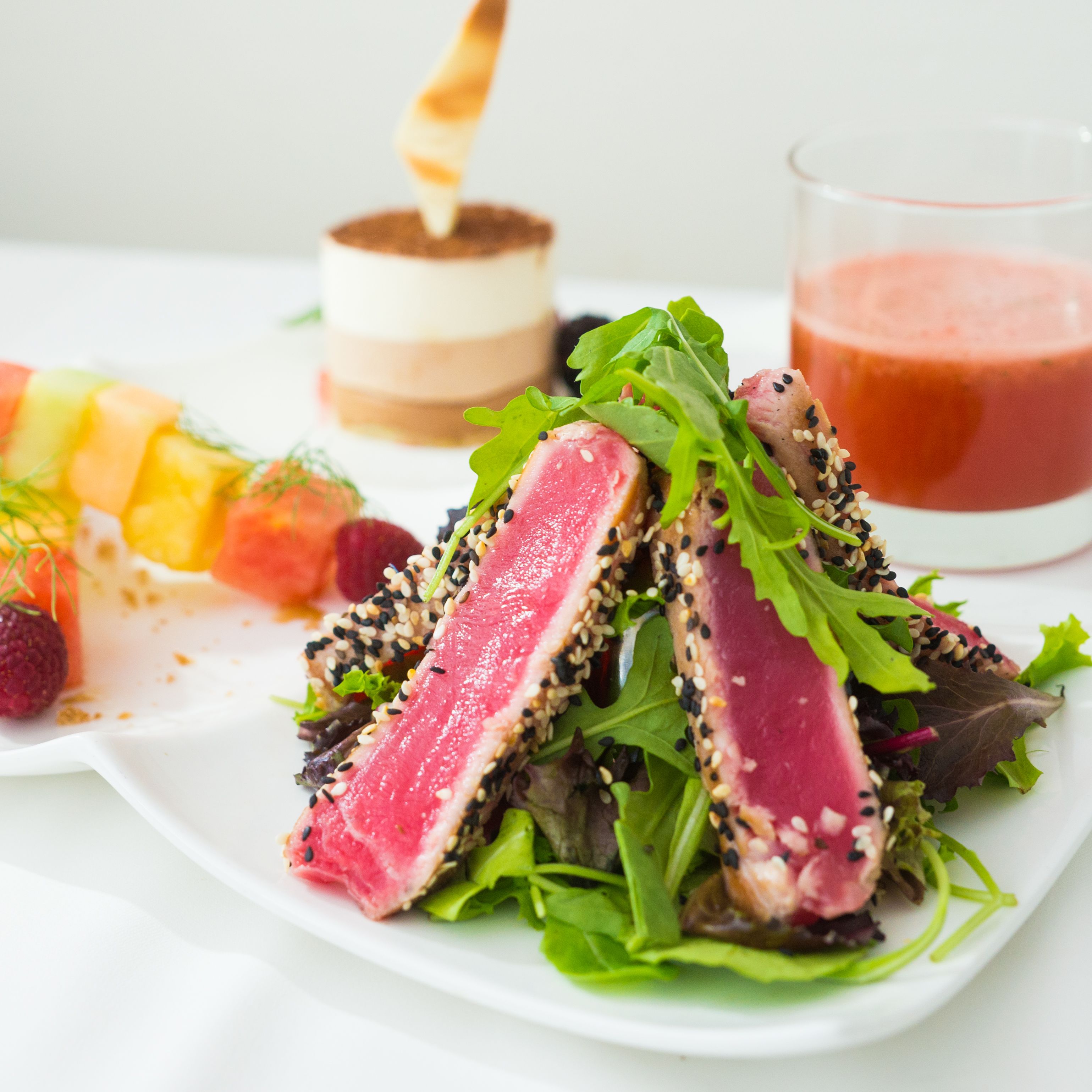 A plate of food with seared tuna, greens, and a dessert.
