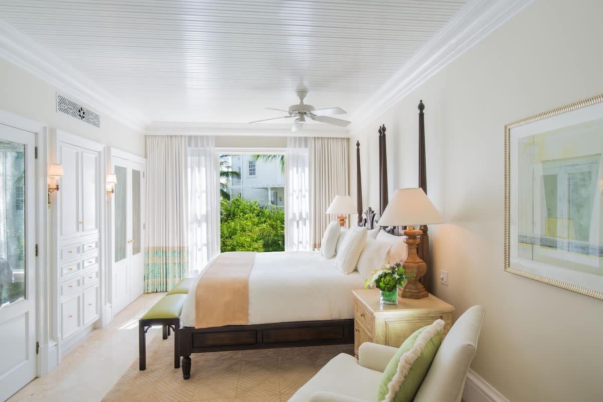 Een ruime slaapkamer met een groot bed, een zithoek en een balkon met uitzicht op groen.