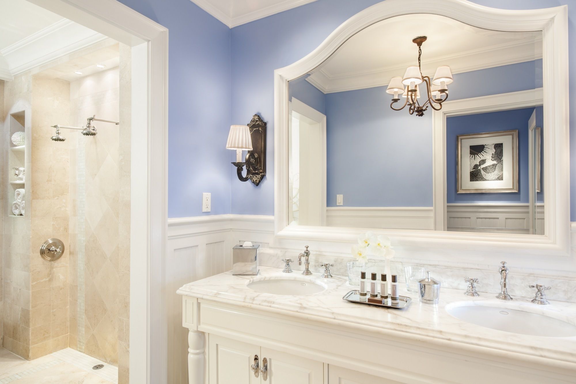 A bathroom with two sinks, a large mirror, a chandelier, and a framed artwork on the wall.