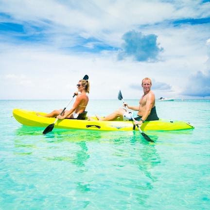 Two people in a yellow kayak on clear turquoise water.