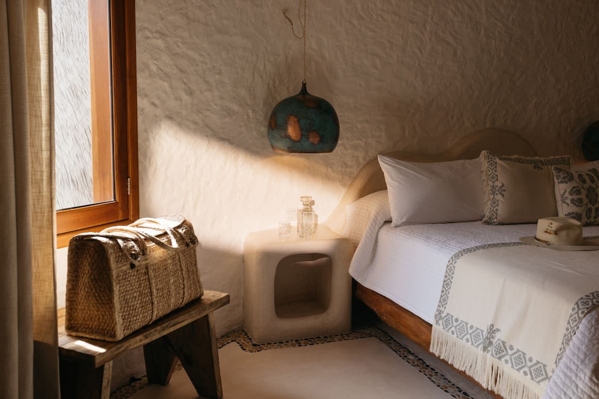 A cozy bedroom with a wooden bed, a small bedside table, a woven basket, and a hanging light fixture.