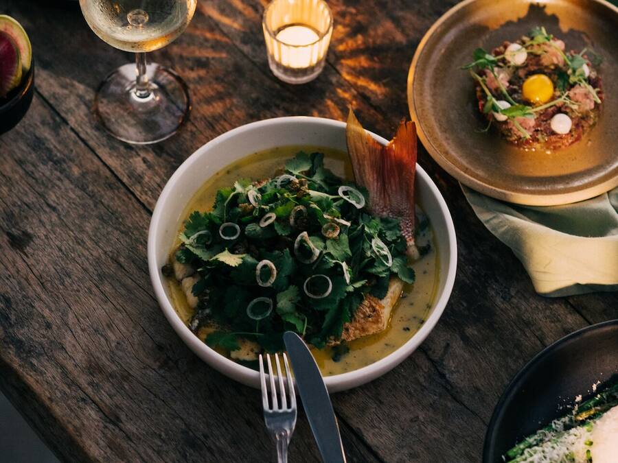 Una mesa de madera con un tazón de sopa adornado con hierbas, un plato de pan y una copa de vino.