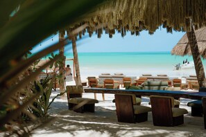 Un salón junto a la playa con techo de paja, mobiliario de madera y vista al océano.
