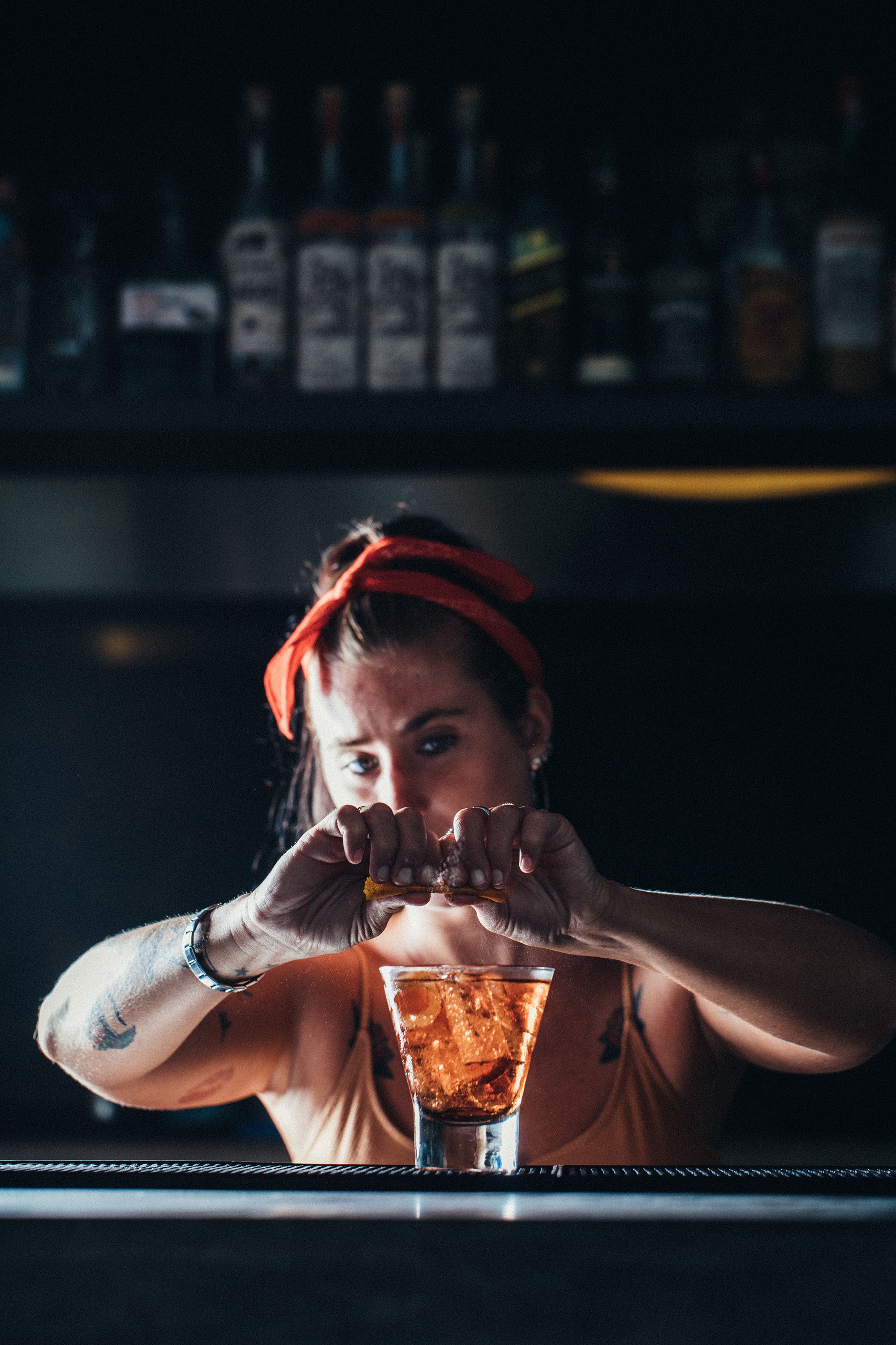 Una persona en un bar, con una bebida delante, rodeada de botellas de alcohol.