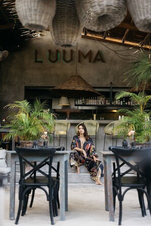 A woman sitting on outdoor steps in a restaurant with a sign reading "LUUMA" in the background.