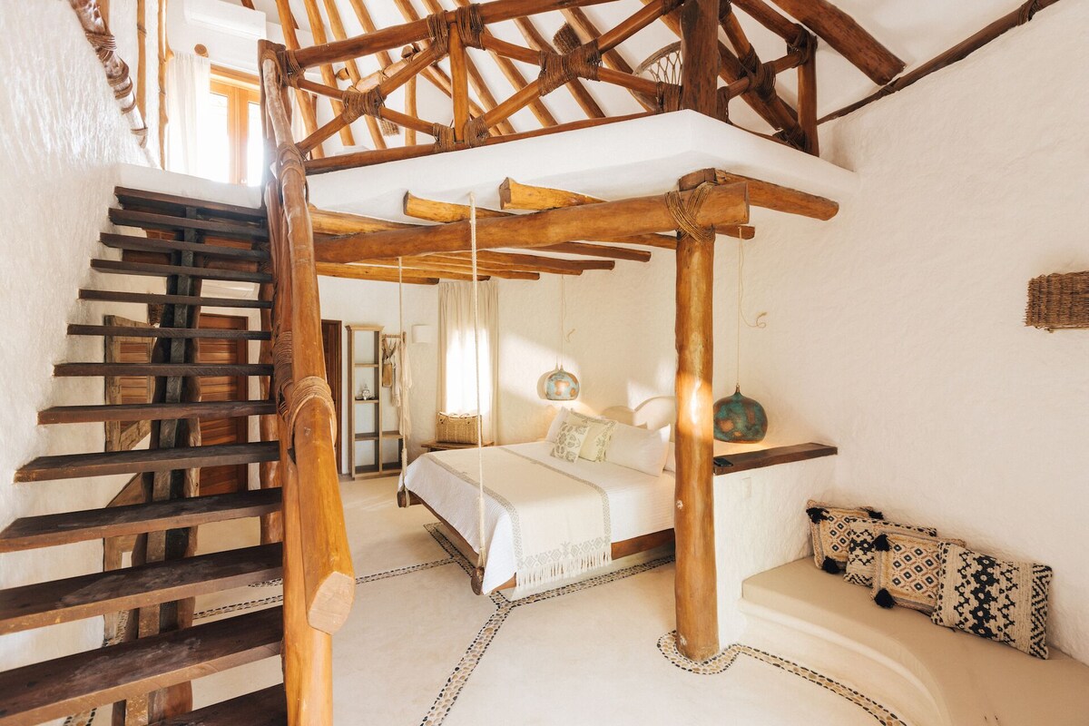 A rustic bedroom with a wooden ladder, a canopy bed, and a small seating area.