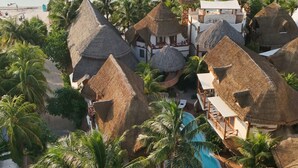 Un resort con edificios de techo de paja, piscina y vista al mar.