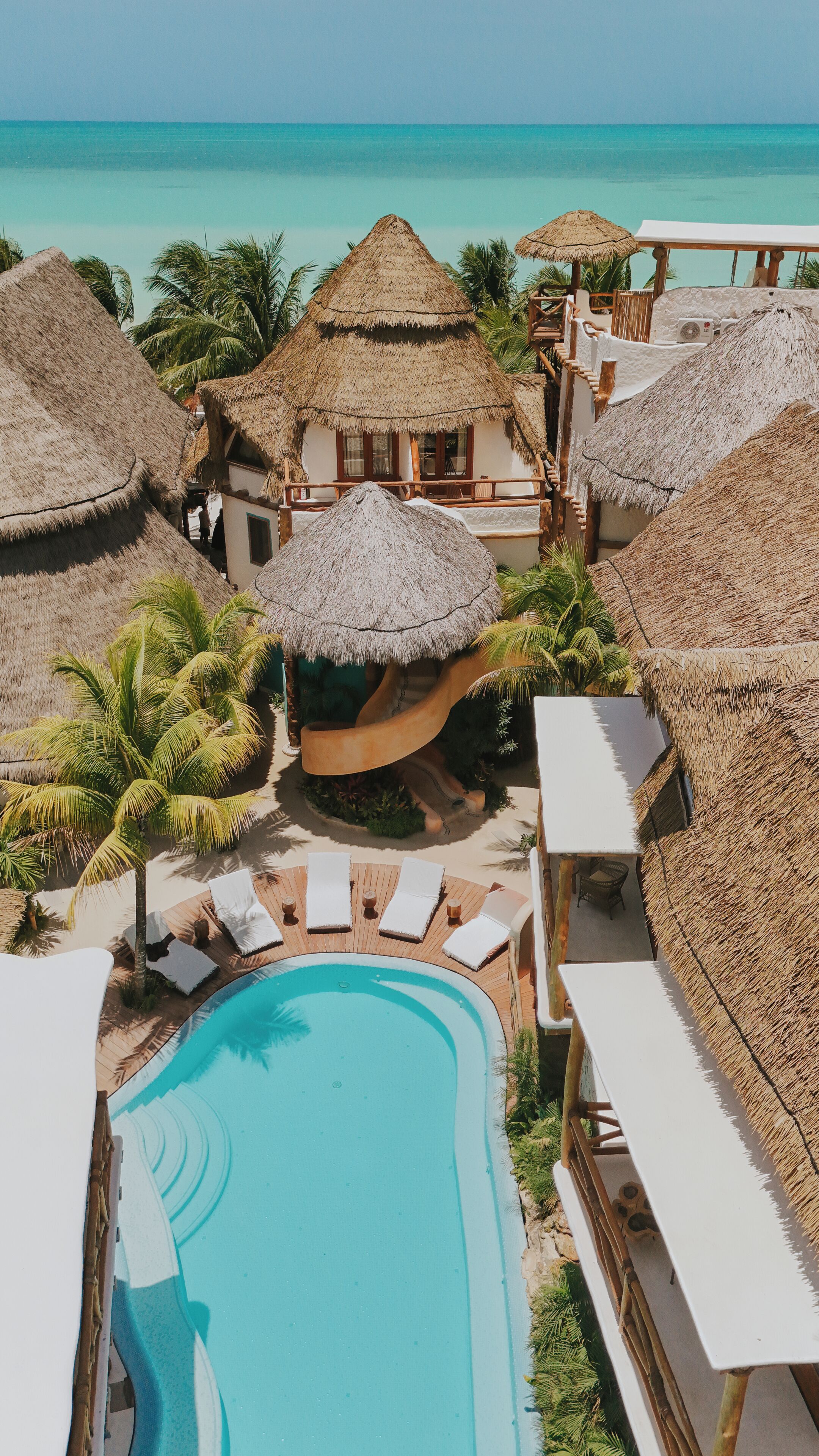 A resort with a swimming pool, thatched-roof structures, and palm trees.