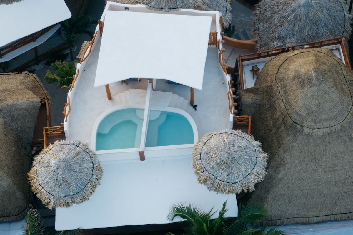 A boat with a pool, surrounded by thatched umbrellas and palm trees.