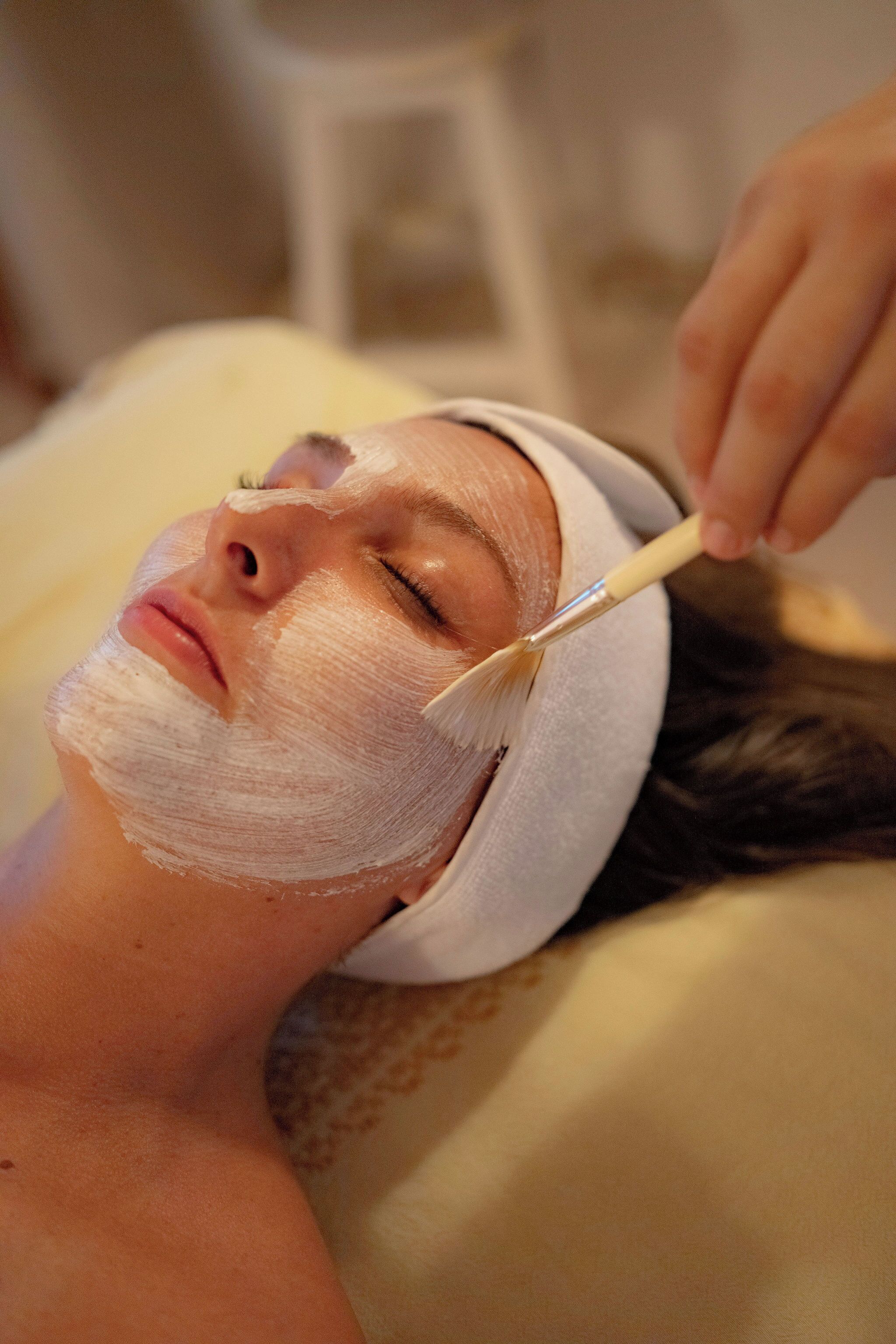 Una persona acostada con una toalla en la cabeza, recibiendo un tratamiento facial.