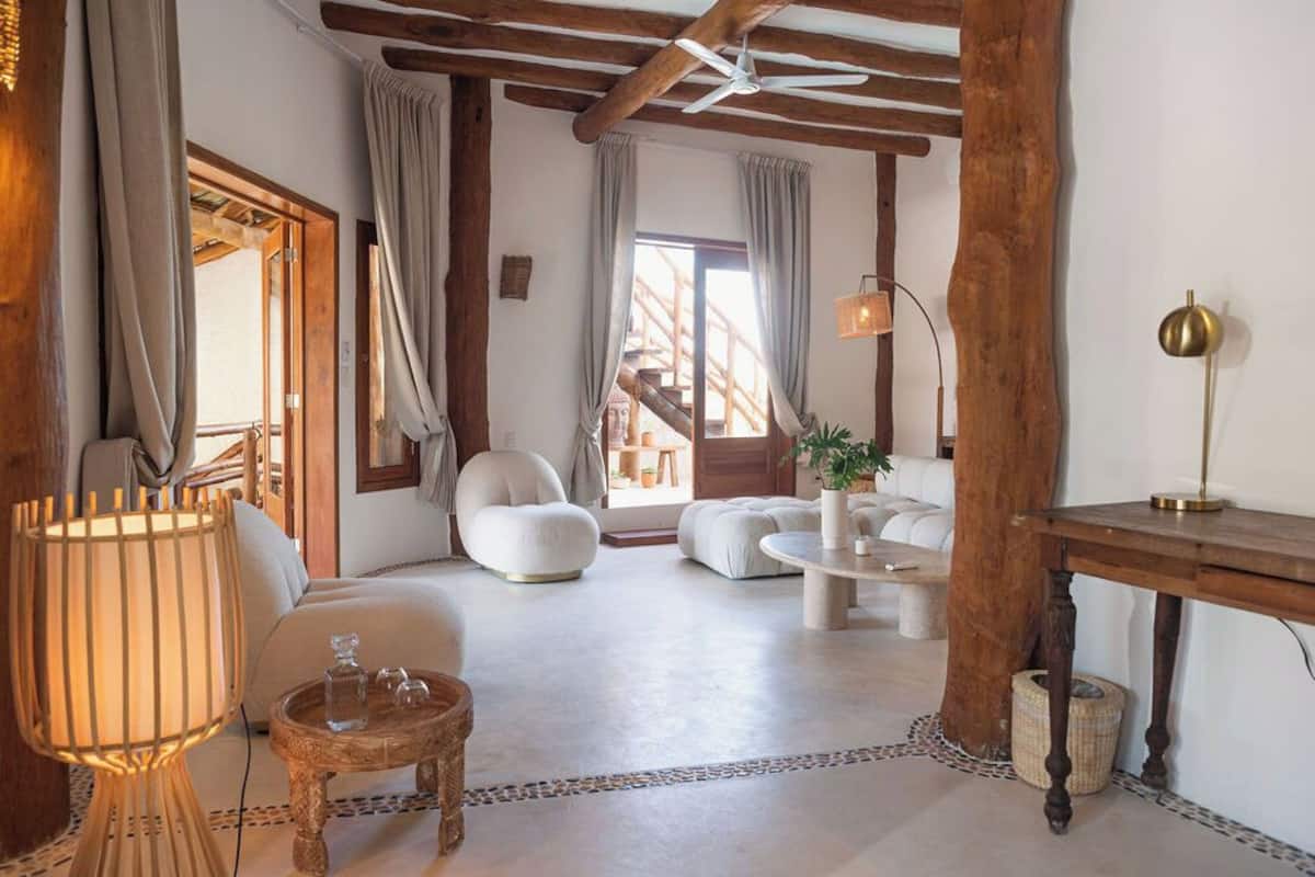 A spacious living room with a high ceiling, wooden beams, a round coffee table, a sofa, and a lamp.