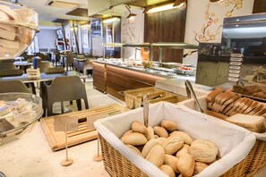 A bakery counter with various breads and pastries, a display of cheeses, and a seating area with tables and chairs. - Hotel Florencio (Sant Antoni de Portmany)