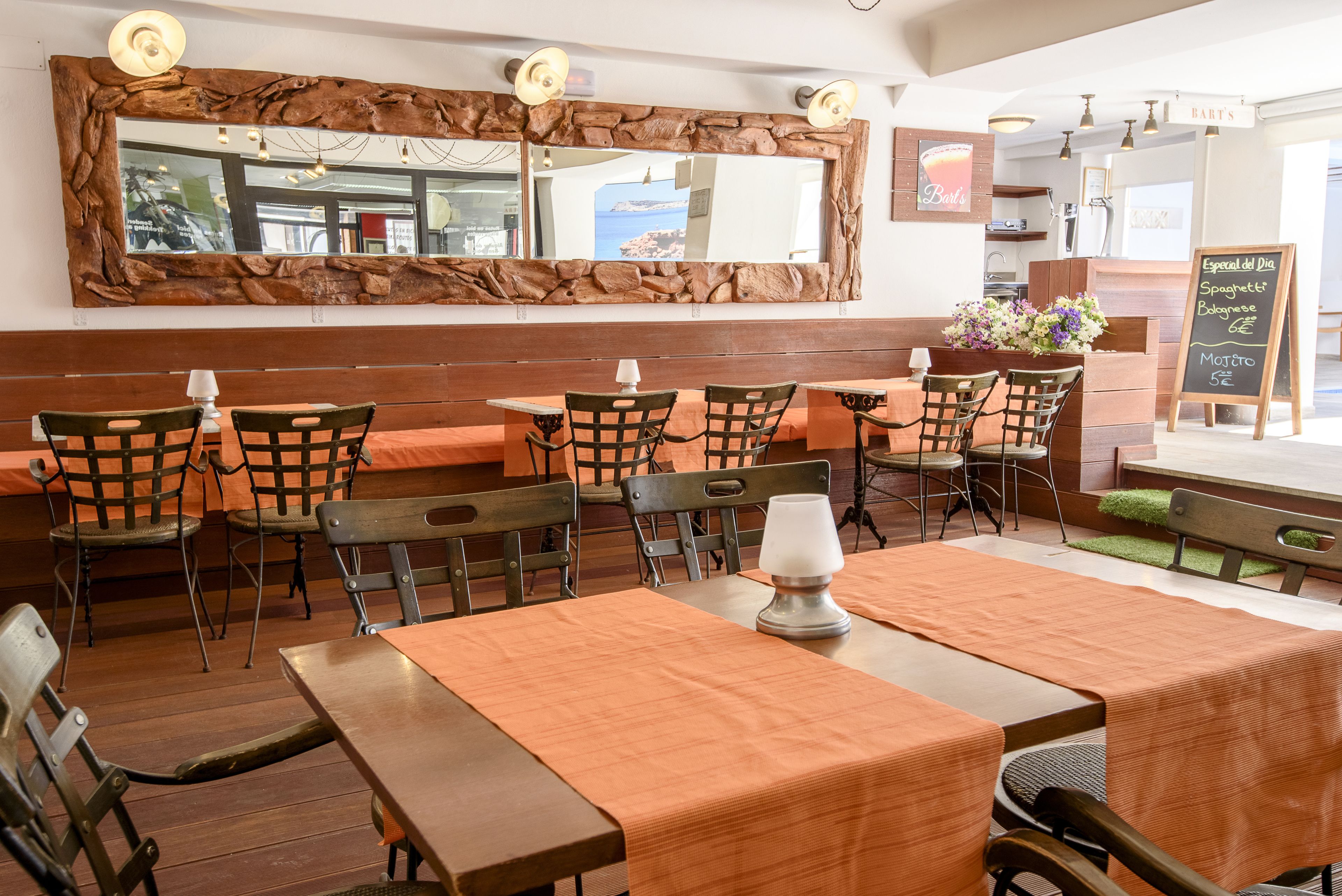Un restaurante con mesas y sillas de madera, un espejo grande con marco rústico y un menú en pizarra.