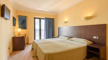 Quarto de hotel com duas camas, uma escrivaninha, uma cadeira, uma televisão, um quadro e uma janela com cortinas.