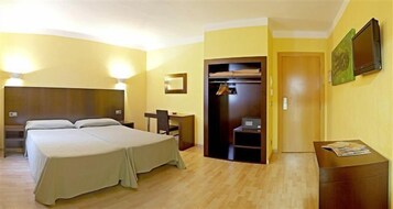 A hotel room with a double bed, a desk with a chair, a wardrobe, and a TV on the wall.