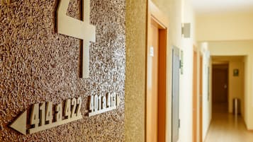 Un couloir avec un mur à texture et un panneau indiquant les numéros des pièces ainsi qu’un numéro de téléphone.