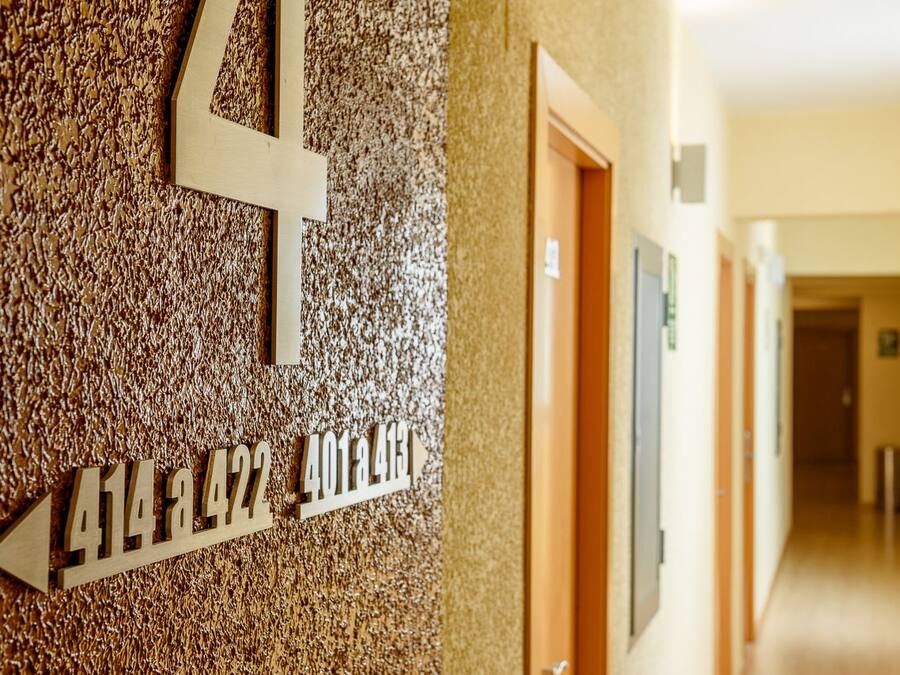Un couloir avec un mur à texture et un panneau indiquant les numéros des pièces ainsi qu’un numéro de téléphone.