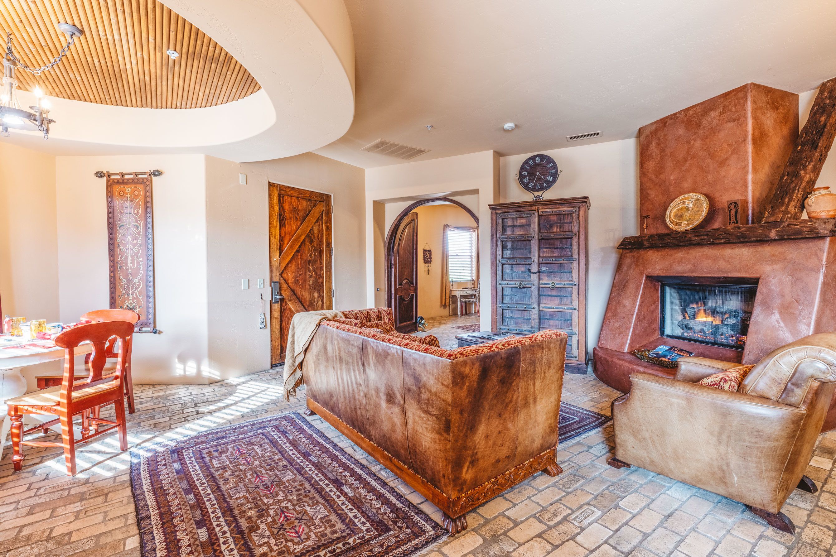 A spacious living room with a fireplace, a large wooden door, and a dining area with a table and chairs.