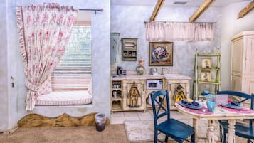 Una cocina acogedora con una mesa de comedor para dos personas, una ventana con cortinas florales y decoración de estilo vintage.