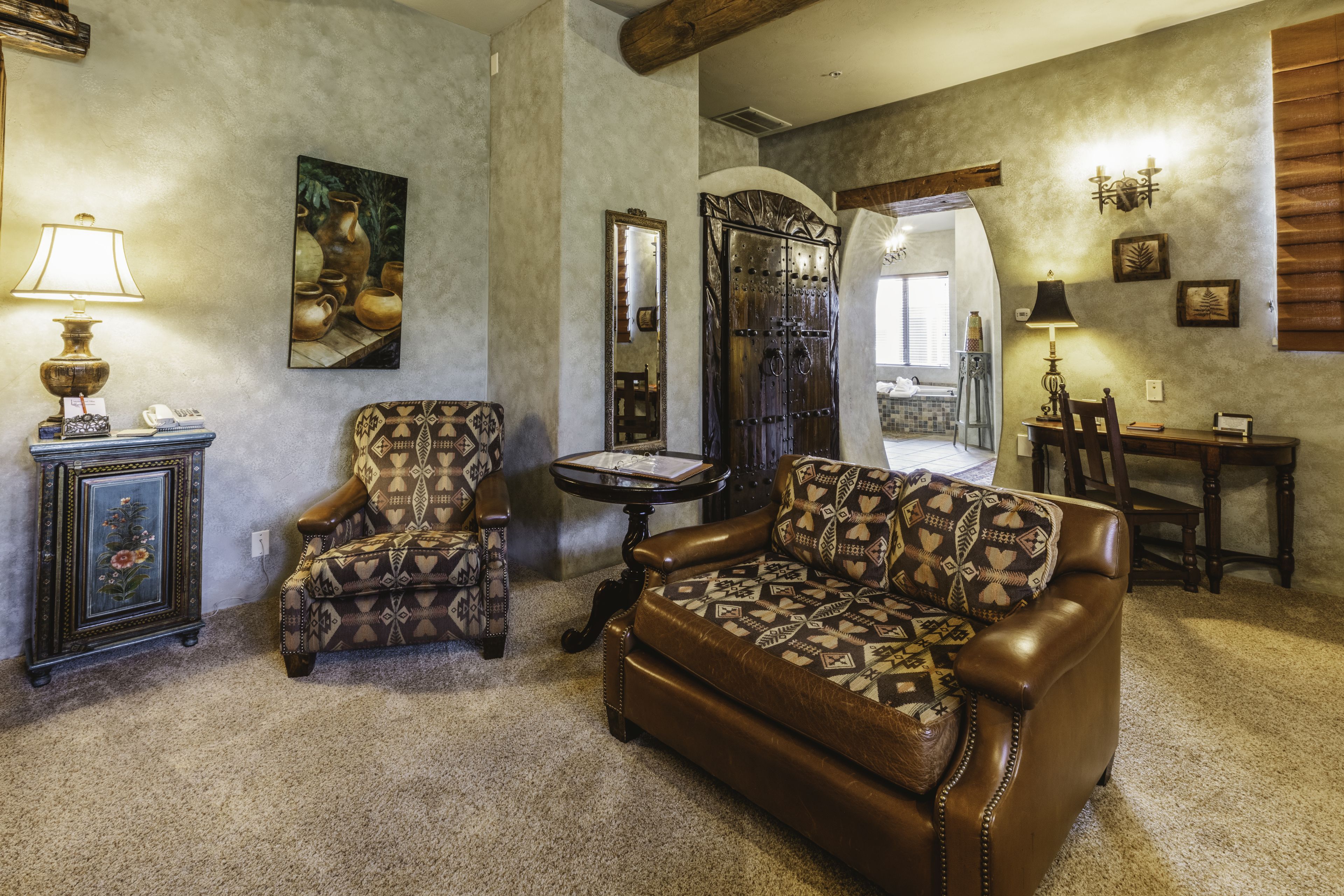 A living room with a brown leather sofa, patterned armchair, and a small round table with a lamp.