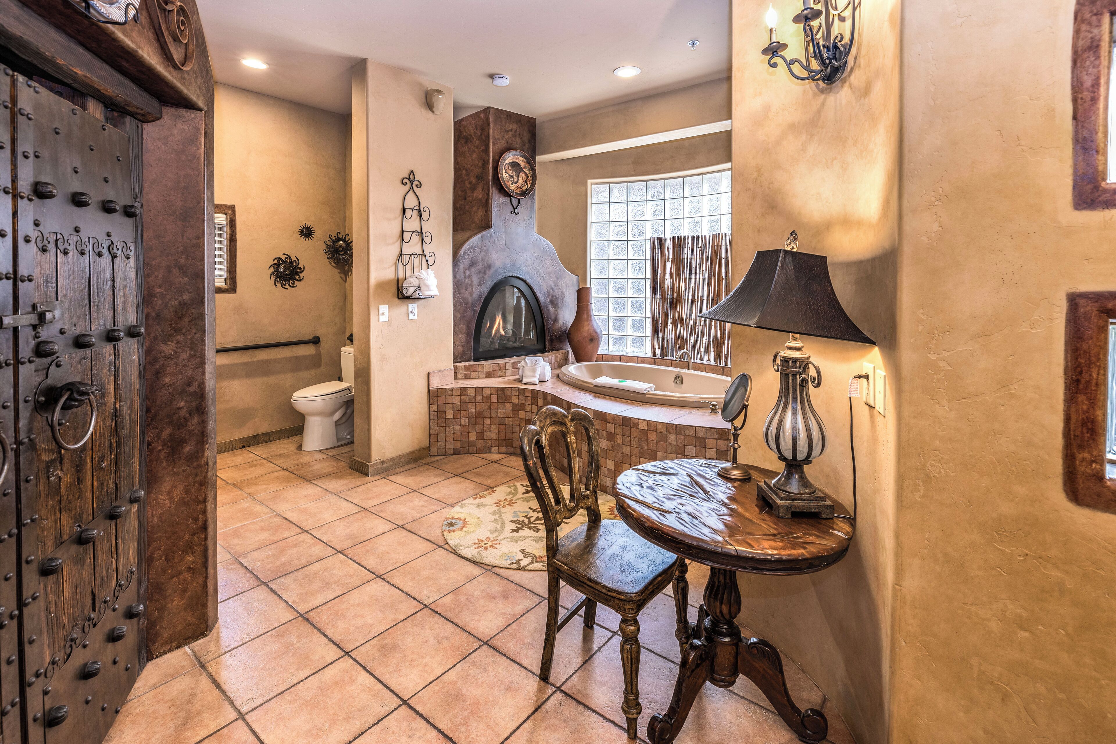 A bathroom with a fireplace, a bathtub, a toilet, and a table with a lamp.
