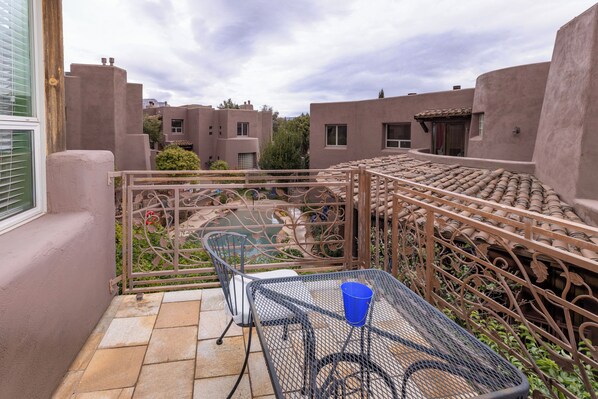 A balcony with a metal table and chair, a blue cup, and a view of neighboring buildings.