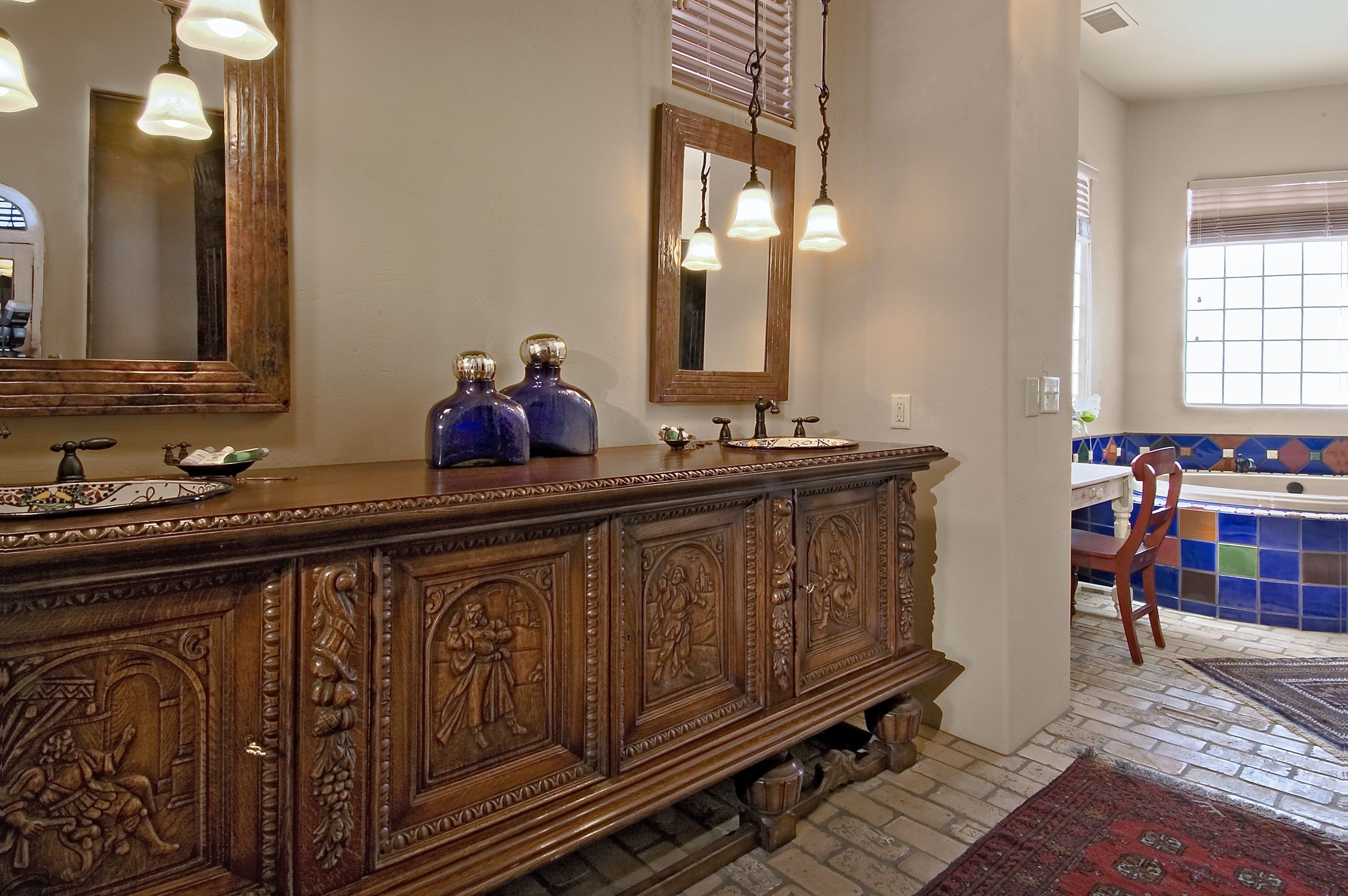 A bathroom with a wooden vanity, two blue vases, a mirror, and a tiled shower area.