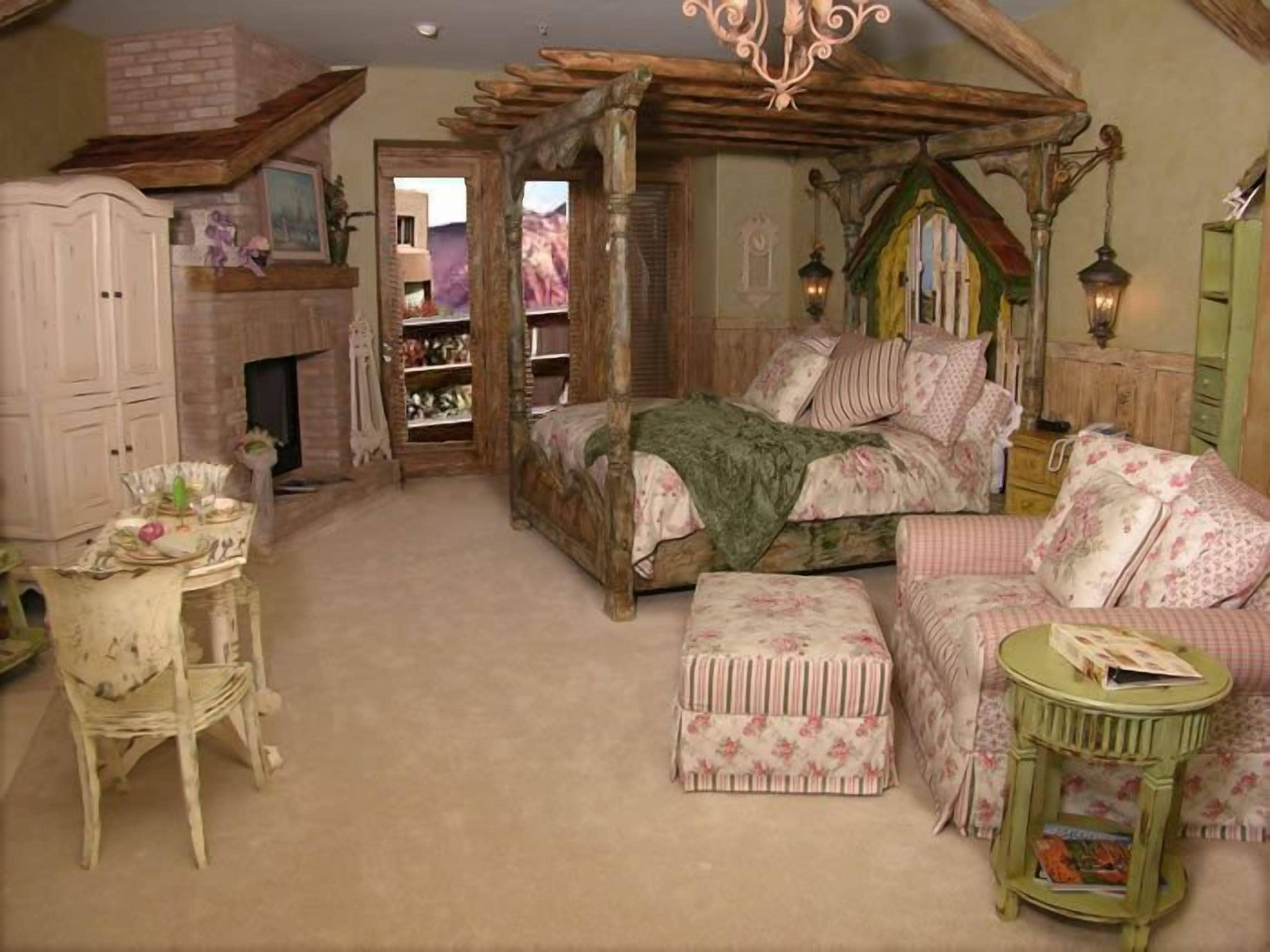 A bedroom with a wooden canopy bed, a small table, a chair, a side table, and a bookshelf.